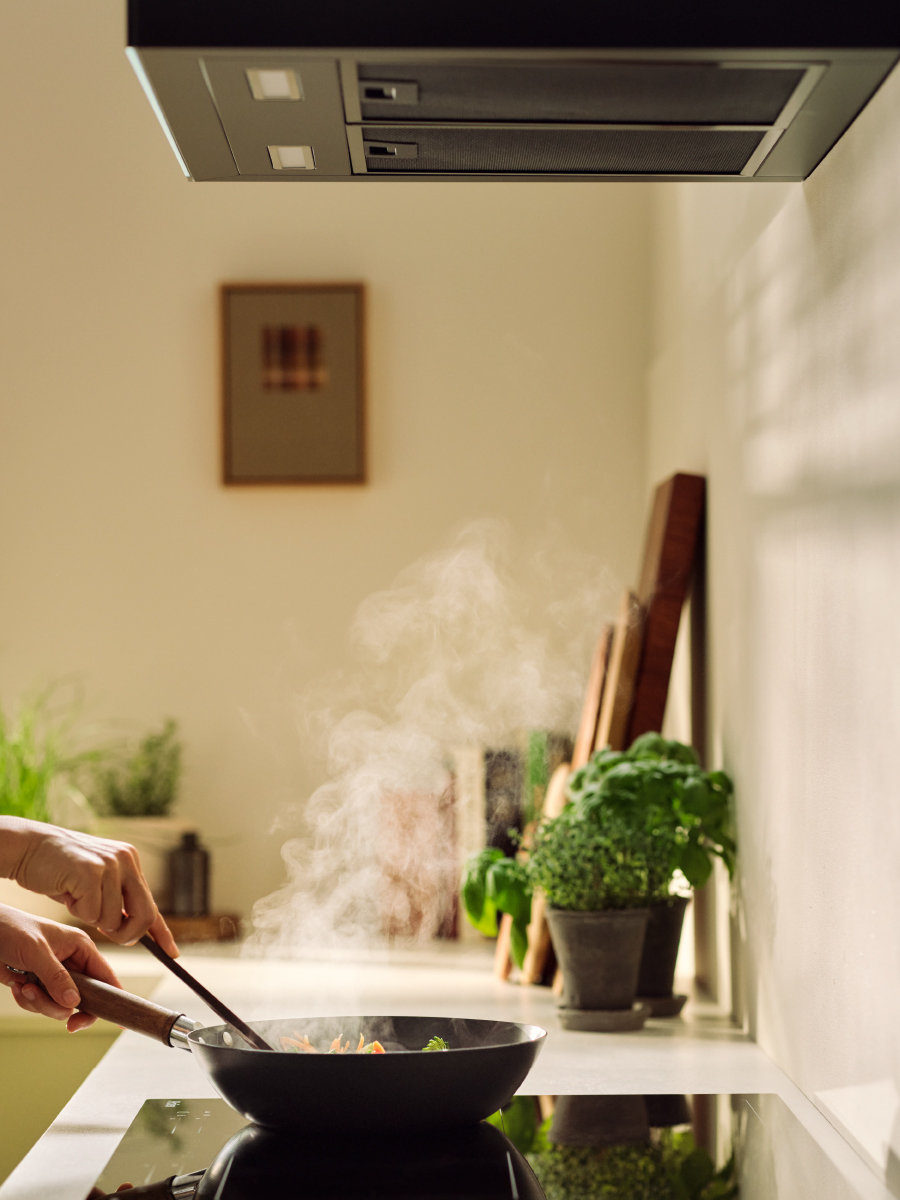 Frypan on a cooktop with steam from food going up to rangehood