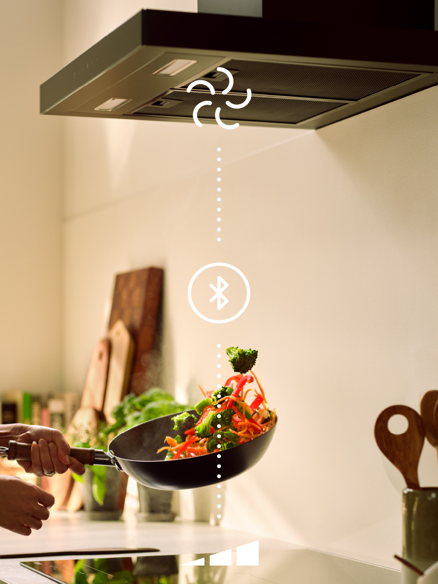 Tossing vegetables in a frying pan underneath a rangehood